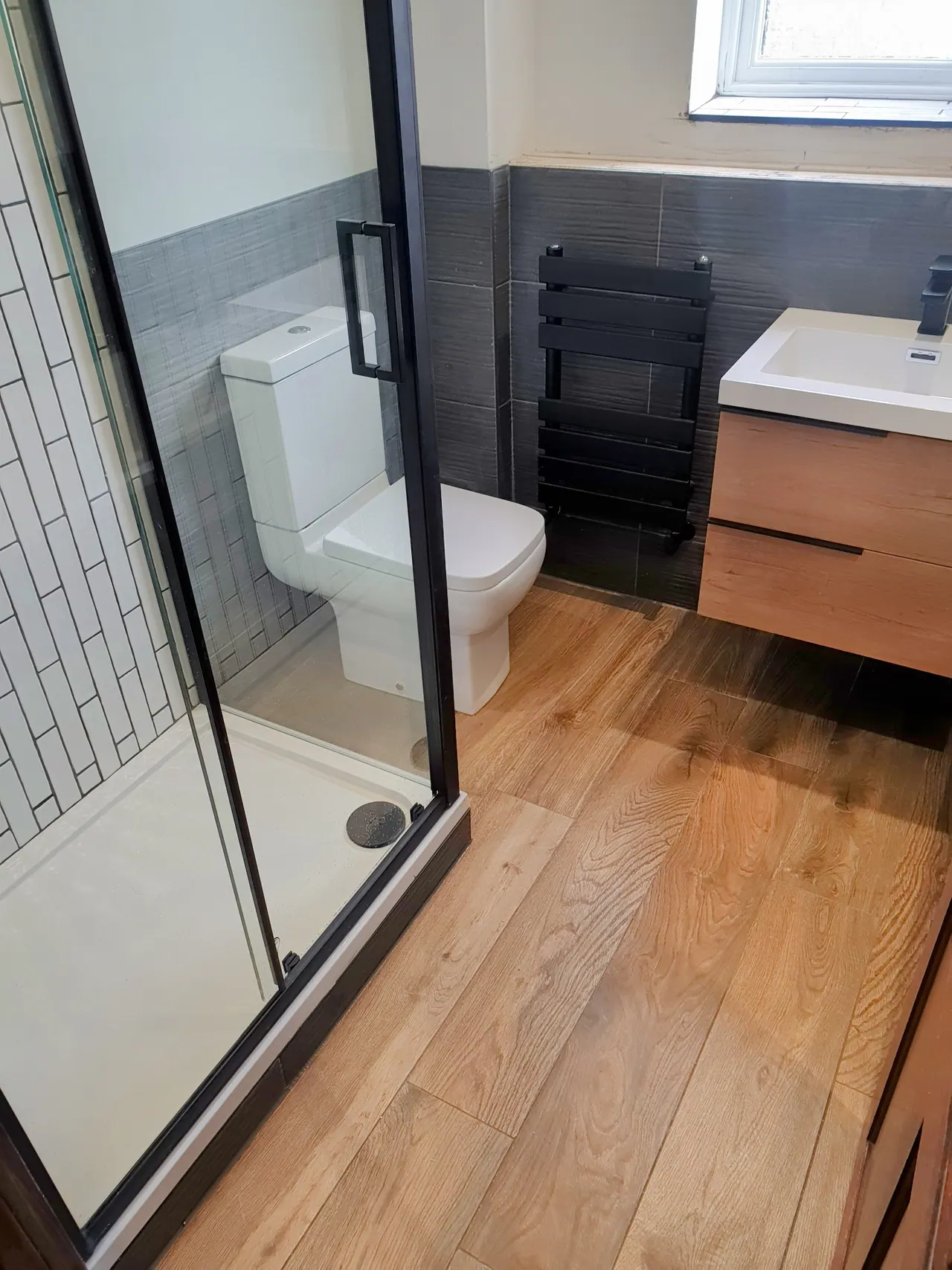 Modern completed shower room with black framed enclosure and timber vanity